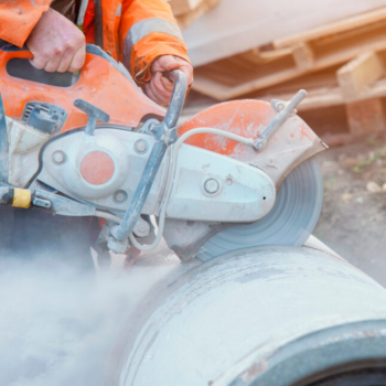 Close up of a construction worker as he saws into a metal pipe.
