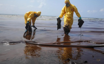 Two workers clean an oil spill while wearing full-body PPE