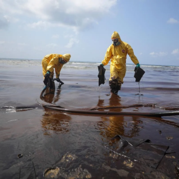Two workers clean an oil spill while wearing full-body PPE