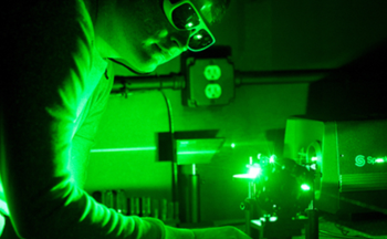 A person wearing safety goggles operates a laser, he is bathed in green light.