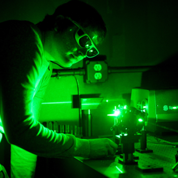 A person wearing safety goggles operates a laser, he is bathed in green light.