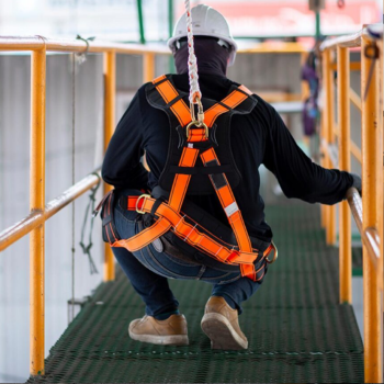 A worker crouches on a catwalk, while wearing fall protection gear.