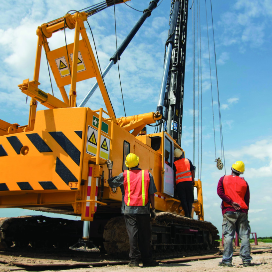 A group of workers wearing PPE are looking up at a large yellow crane