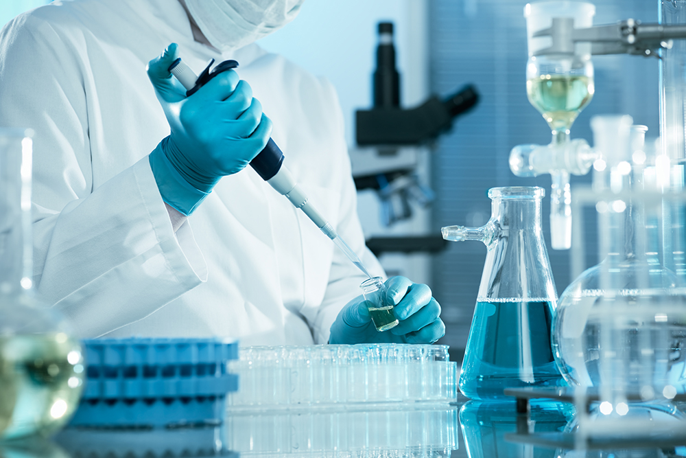 A researcher wearing protective gear takes a sample of a liquid in a laboratory.